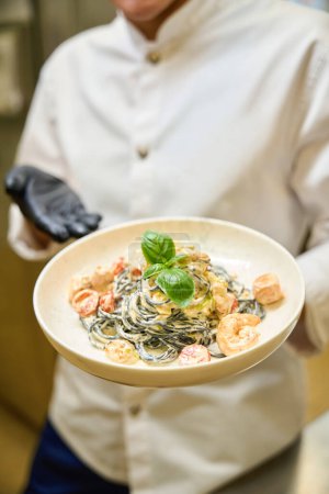 Photo for Cook presents spaghetti in cream sauce, he works in protective gloves - Royalty Free Image