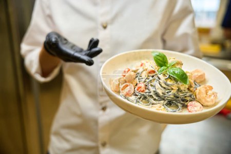 Foto de Chef presenta la tradicional porción de espaguetis en salsa de crema, trabaja con guantes protectores - Imagen libre de derechos