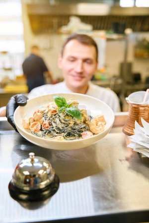 Téléchargez les photos : Employé de cuisine passe spaghetti dans une sauce spéciale à la salle, il travaille dans des gants de protection - en image libre de droit