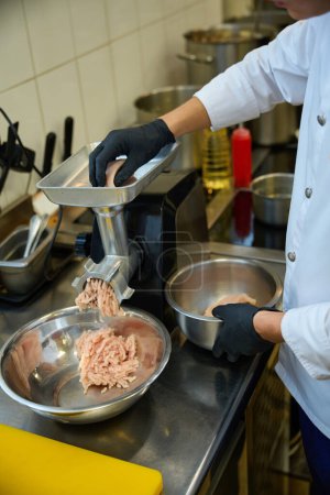 Téléchargez les photos : Le personnel de cuisine broie la viande dans une broyeuse à viande, un homme travaille avec des gants de protection - en image libre de droit