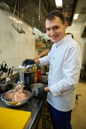 Téléchargez les photos : Il broie de la viande dans une broyeuse à viande, il travaille avec des gants de protection - en image libre de droit
