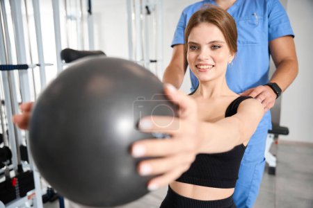 Photo for Woman performing exercises with a ball under the supervision of a physiotherapist, woman in a training suit - Royalty Free Image