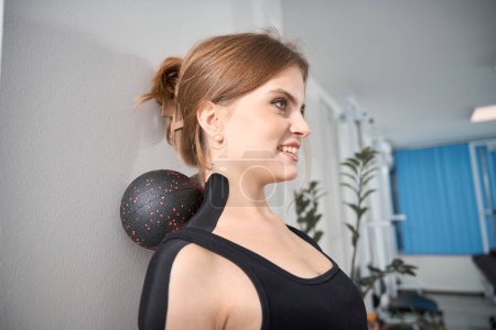Foto de Hermosa mujer realiza ejercicios contra la pared con un dispositivo especial, hembra en un traje de entrenamiento cómodo - Imagen libre de derechos
