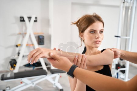 Photo for Physiotherapist helping female patient perform stretching exercises for arm muscles, woman wearing comfortable black clothes - Royalty Free Image