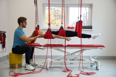Foto de Hombre fija a una mujer en un sistema de bucle suspendido en una cuerda roja, se utiliza una técnica de curación moderna - Imagen libre de derechos