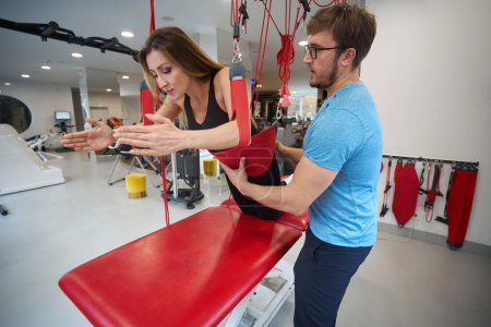 Téléchargez les photos : Employé d'une clinique de réadaptation travaille avec un patient sur un cordon rouge, en utilisant un équipement moderne - en image libre de droit