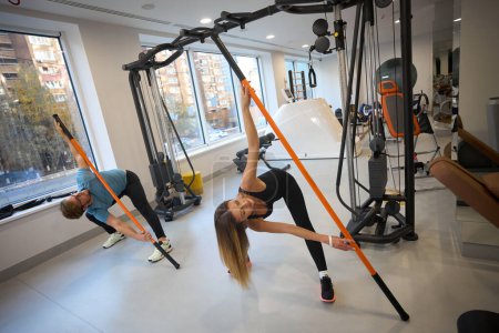Foto de Hombre y mujer en ropa de entrenamiento realizan ejercicios físicos en el gimnasio, se utilizan palos deportivos - Imagen libre de derechos