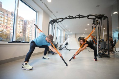 Foto de Mujer y hombres realizan ejercicios de estiramiento, utilizan palos deportivos especiales - Imagen libre de derechos