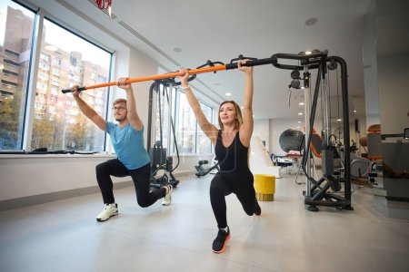 Photo for Beautiful woman and man are doing a warm-up with a special stick, they are working out in a modern gym - Royalty Free Image
