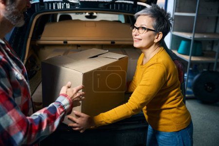 Photo for Woman takes a box of things out of the trunk of a car - Royalty Free Image