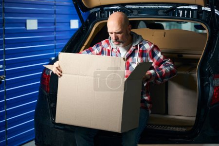 Photo for Man in a plaid shirt holds a large cardboard box on his lap - Royalty Free Image