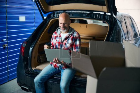 Photo for Guy sits with a laptop in his hands around cardboard boxes - Royalty Free Image