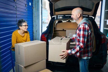 Photo for Adult man takes cardboard boxes from the trunk of a car while moving - Royalty Free Image
