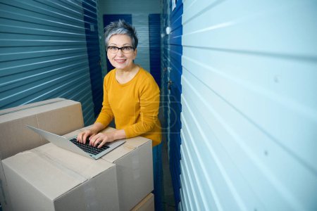Téléchargez les photos : Femme se tient avec un ordinateur portable sur des boîtes en carton pour le transport des choses - en image libre de droit