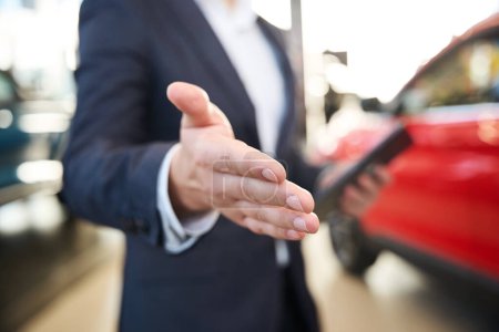 Photo for Car dealer with a tablet in his hands extends his hand to make a deal - Royalty Free Image
