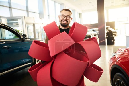 Photo for Young man in glasses holding a beautiful red gift decorative bow - Royalty Free Image