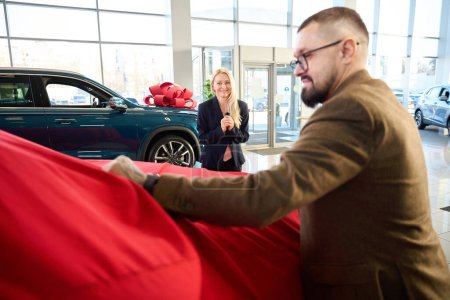 Photo for Woman was delighted as her husband removed the red cover from the new car - Royalty Free Image