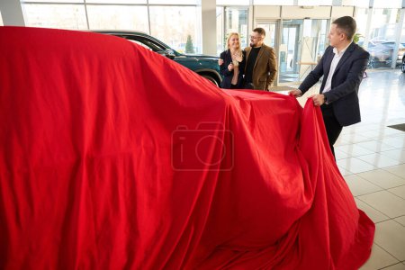 Photo for Car salesman removes the red sheet from a new car - Royalty Free Image