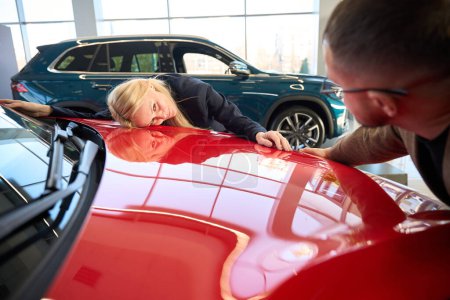 Foto de Mujer rubia se encuentra en la capucha de su nuevo coche comprado - Imagen libre de derechos