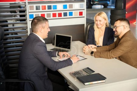 Foto de Dos compradores y un vendedor están sentados en una mesa frente a un documento de compra de coche - Imagen libre de derechos
