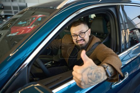 Photo for Man with glasses shows thumbs up while sitting in the interior of a new car - Royalty Free Image