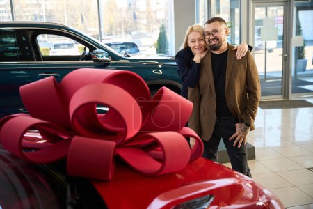 Téléchargez les photos : Mari et femme regardent joyeusement leur nouvelle voiture rouge - en image libre de droit