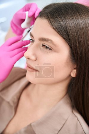 Téléchargez les photos : Esthéticienne en gants roses debout près du patient, tenant une seringue et faisant une injection faciale à la clinique - en image libre de droit