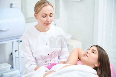 Photo for Female customer lying on couch in beauty salon, cosmetologist sitting near and making injection in arm - Royalty Free Image