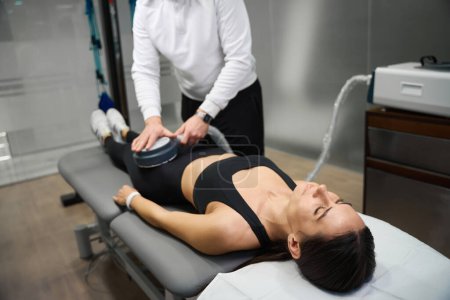 Foto de Terapia magnética. Dispositivo magnético de sujeción masculino profesional, haciendo el procedimiento para la mujer en el sofá - Imagen libre de derechos