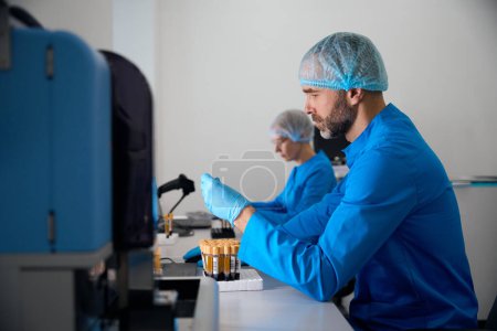Male in the laboratory works with blood samples, his colleague works nearby