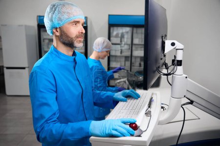 Foto de El virólogo masculino y su colega utilizan un aparato especial para el aislamiento automático de ácidos nucleicos, personas en uniformes azules - Imagen libre de derechos