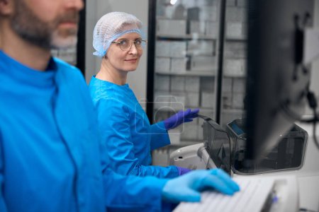 Foto de Los virólogos utilizan un aparato especial para el aislamiento automático de ácidos nucleicos, personas en uniformes azules - Imagen libre de derechos
