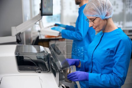 Personal de laboratorio utiliza un aparato especial para el aislamiento automático de ácidos nucleicos, personas en uniformes azules