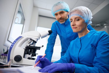 Téléchargez les photos : Femme et homme sur le lieu de travail dans un laboratoire moderne, un microscope puissant est utilisé - en image libre de droit