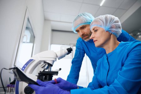 Mann und Frau am Arbeitsplatz im modernen Labor, leistungsstarkes Mikroskop wird verwendet