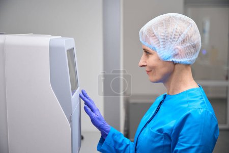 Foto de Ayudante de laboratorio femenina trabaja en un laboratorio en equipos modernos, una mujer en uniforme azul - Imagen libre de derechos