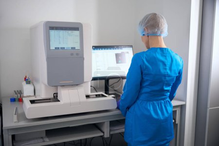 Photo for Woman immunologist enters work data into the database, there is modern equipment in the laboratory - Royalty Free Image