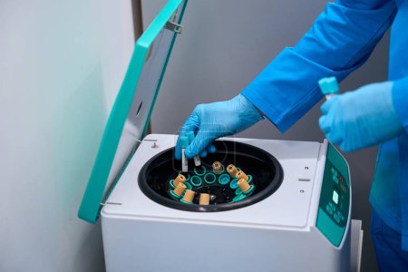 Foto de Asistente de laboratorio coloca tubos de ensayo con biomaterial en un aparato especial, la habitación se mantiene estéril - Imagen libre de derechos
