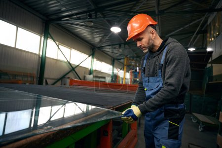 Photo for Worker works with a large piece of glass in a window production, a man wearing protective gloves - Royalty Free Image