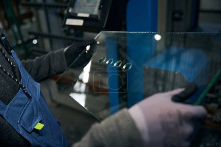 Meister hält gebohrtes Glas für ein doppelt verglastes Fenster in der Hand, moderne High-Tech-Geräte werden in der Produktion eingesetzt