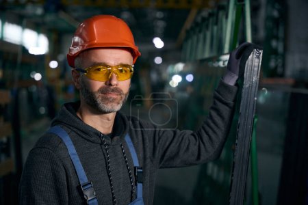 Téléchargez les photos : Employé travaille dans une production de fenêtres avec verre pour les unités à double vitrage, un homme portant des lunettes de sécurité - en image libre de droit