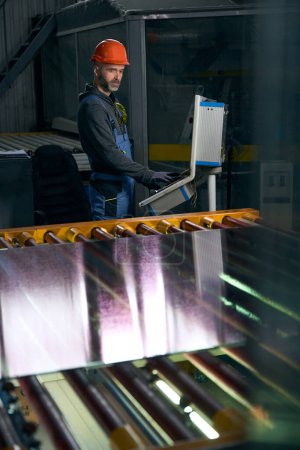 Foto de Trabajador en un taller trabaja con material para ventanas de doble acristalamiento, un hombre en mono de trabajo - Imagen libre de derechos