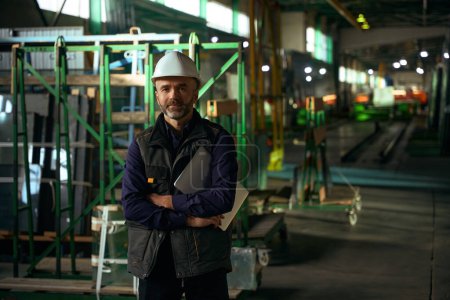 Téléchargez les photos : Homme avec un dossier se tient dans un atelier de production, il porte un casque de protection - en image libre de droit