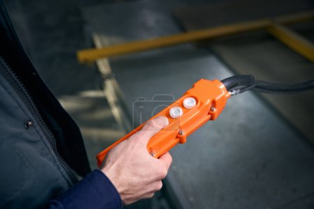 Arbeiter in der Werkstatt hält ein Bedienfeld für ein Produktionsgerät in der Hand, eine orangefarbene Fernbedienung