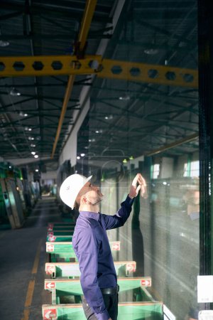 Téléchargez les photos : Ingénieur inspecte le verre dans un atelier de production, l'équipement de haute technologie est utilisé dans la production de fenêtres - en image libre de droit