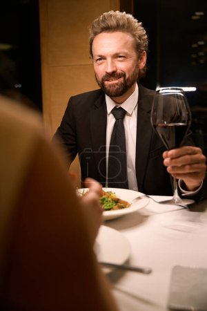Foto de El hombre hace un brindis en la cena en un restaurante, su compañero está sentado enfrente - Imagen libre de derechos
