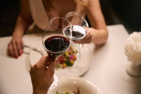 Téléchargez les photos : Couple dégustant du vin rouge pendant le dîner dans un restaurant, servi avec une salade légère - en image libre de droit