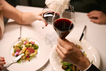 Foto de Pareja bebiendo vino tinto en la cena en el restaurante, ensalada ligera servida - Imagen libre de derechos