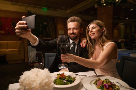 Foto de Hermosa pareja toma una selfie en un restaurante, una dama en un vestido de noche - Imagen libre de derechos