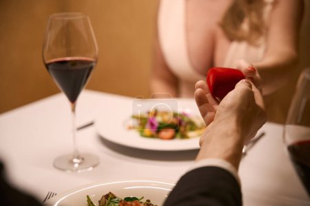 Foto de Compañero le da a la dama una pequeña caja roja, la pareja se sienta en una mesa en un restaurante - Imagen libre de derechos